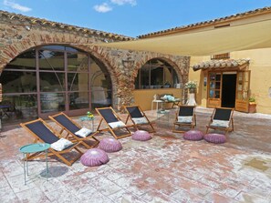 A patio with sun loungers and a small table, surrounded by stone arches and a yellow building. - Hotel&golf Ca La Caputxeta - Adults Only (Castello d'Empuries)
