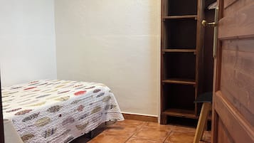 Une petite pièce bien éclairée, avec un lit, une porte en bois et un sol carrelé.