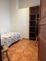 Una habitación pequeña y bien iluminada con una cama, una puerta de madera y piso de baldosas.