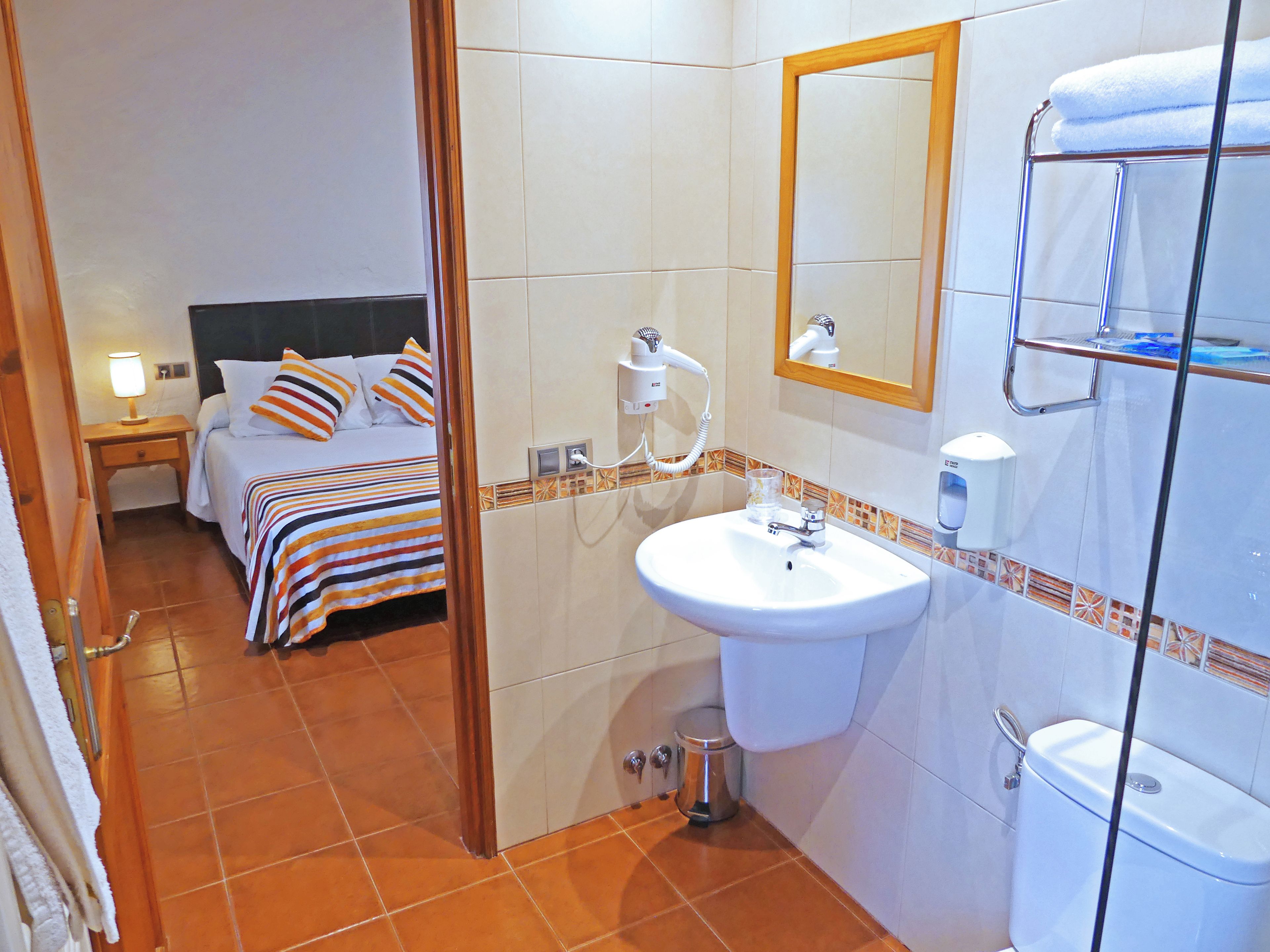 A hotel room with a bed, bedside table, lamp, and a bathroom with a sink, mirror, and towel rack.