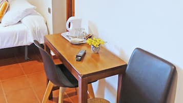 Una habitación con una cama, una mesa con un control remoto, una jarrón y una taza.