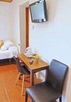 Una habitación con una cama, una mesa con un control remoto, una jarrón y una taza.