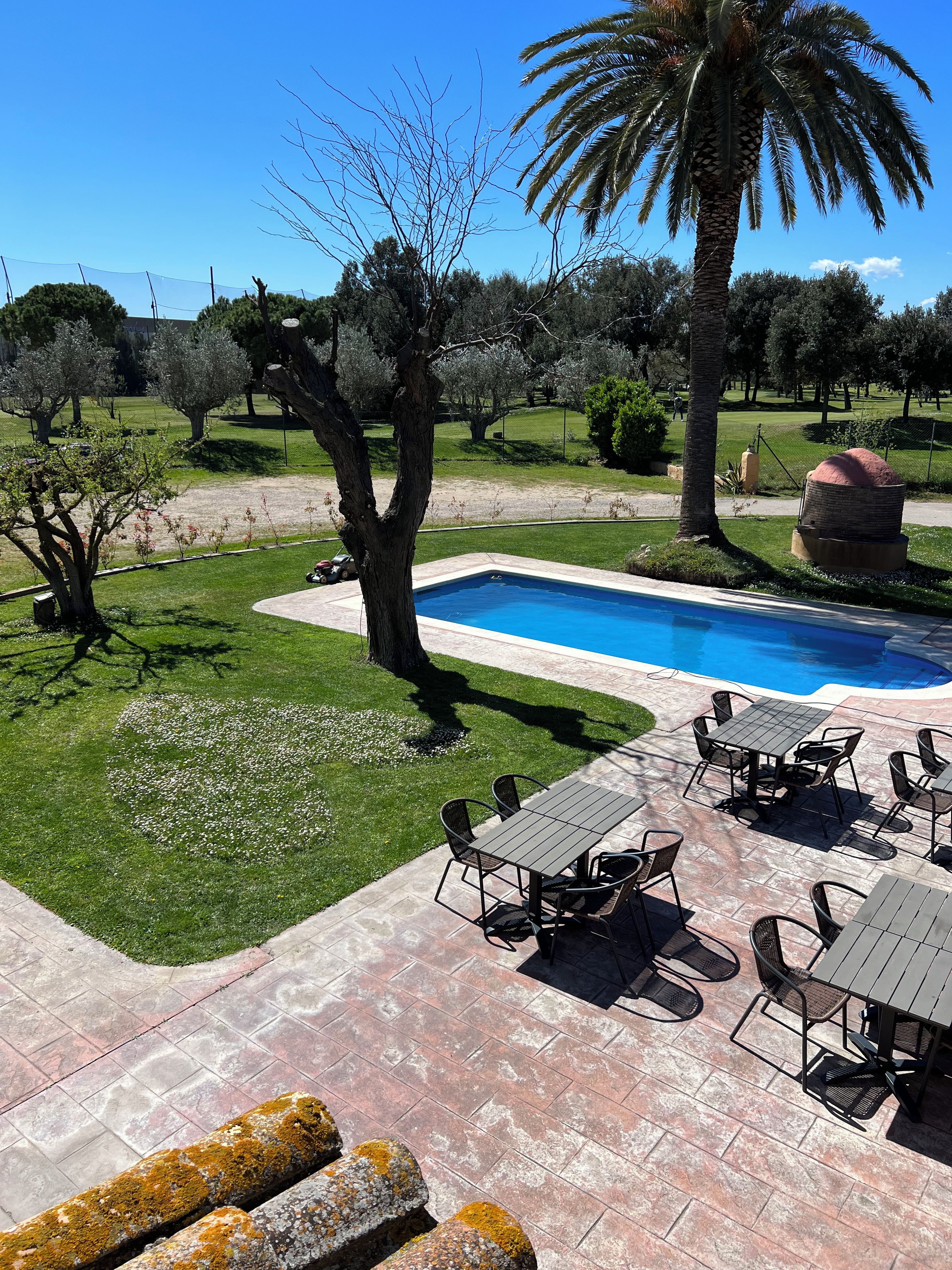 Un área de piscina con terraza, mobiliario exterior y vegetación circundante.