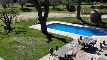 Un área de piscina con terraza, mobiliario exterior y vegetación circundante.