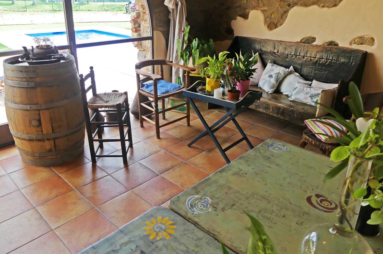 A rustic interior with a wooden barrel, a wooden chair, a sofa with cushions, and a table with potted plants.
