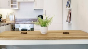 Una cocina moderna con armarios blancos, encimera de madera y dos taburetes blancos.