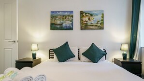 Habitación de hotel con cama, dos cuadros, dos lámparas de noche y toallas enrolladas en el suelo.