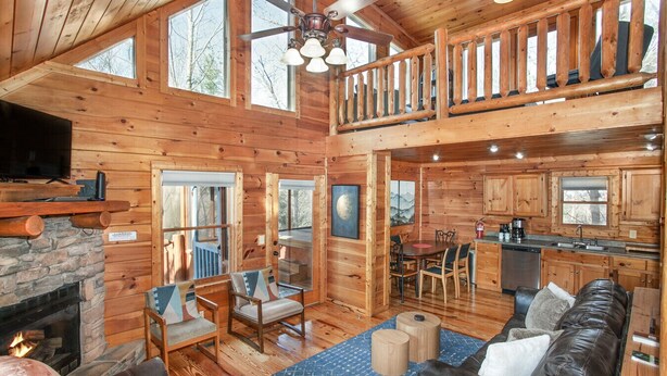 A spacious cabin with a stone fireplace, a dining area, a kitchen, and a balcony with a wooden railing. - Blue Mist Lodge: Hot Tub, Outdoor Lounge, MORE (Sevierville)