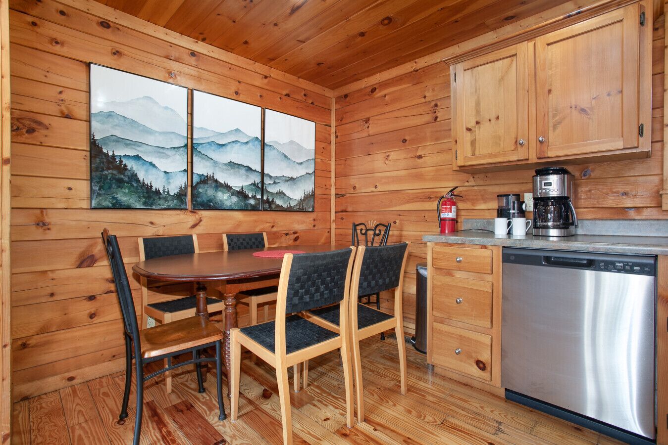 Interior de uma cabana de madeira com mesa de jantar, cadeiras, cafeteira e máquina de lavar louça.