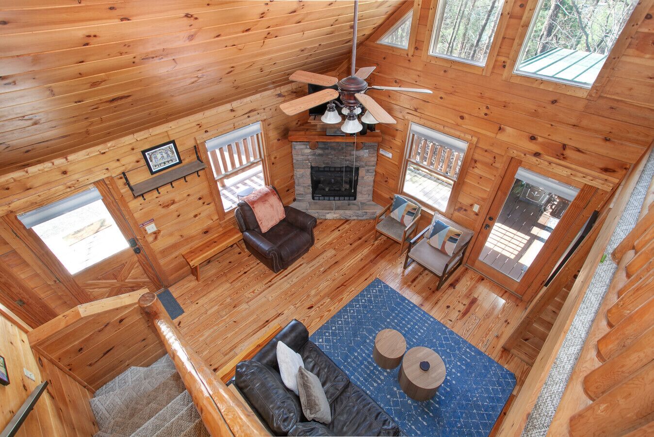 A wooden cabin interior with a fireplace, a ceiling fan, and a seating area with a sofa and chairs.