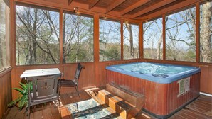 A wooden deck with a hot tub, a table, and chairs, surrounded by large windows. - Blue Mist Lodge: Hot Tub, Outdoor Lounge, MORE (Sevierville)
