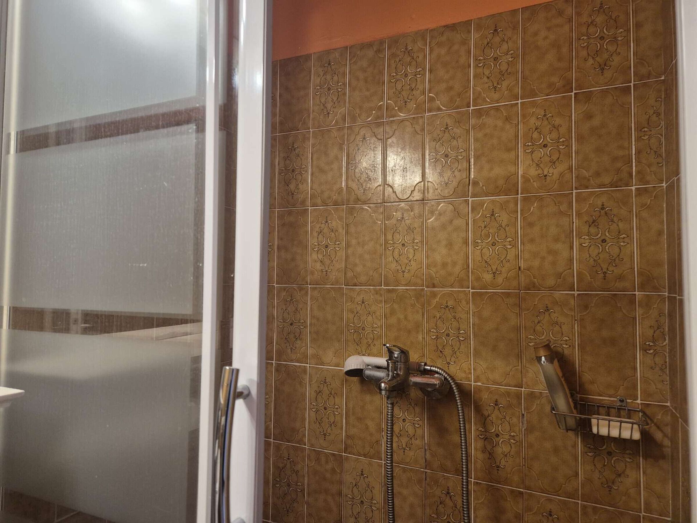 A bathroom with a shower, a glass door, and decorative tiles.