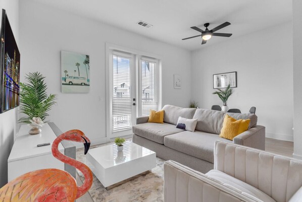 A modern living room with a sofa, coffee table, and a flamingo sculpture. - Beach Bliss: Modern 3 Bed Oasis Mins from Shore (Apollo Beach)