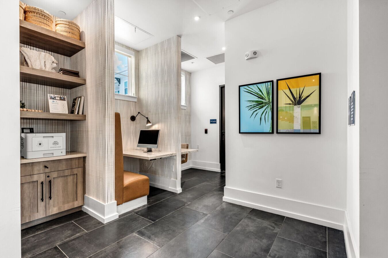 Una oficina en casa moderna con escritorio, computadora y estanterías con objetos decorativos.