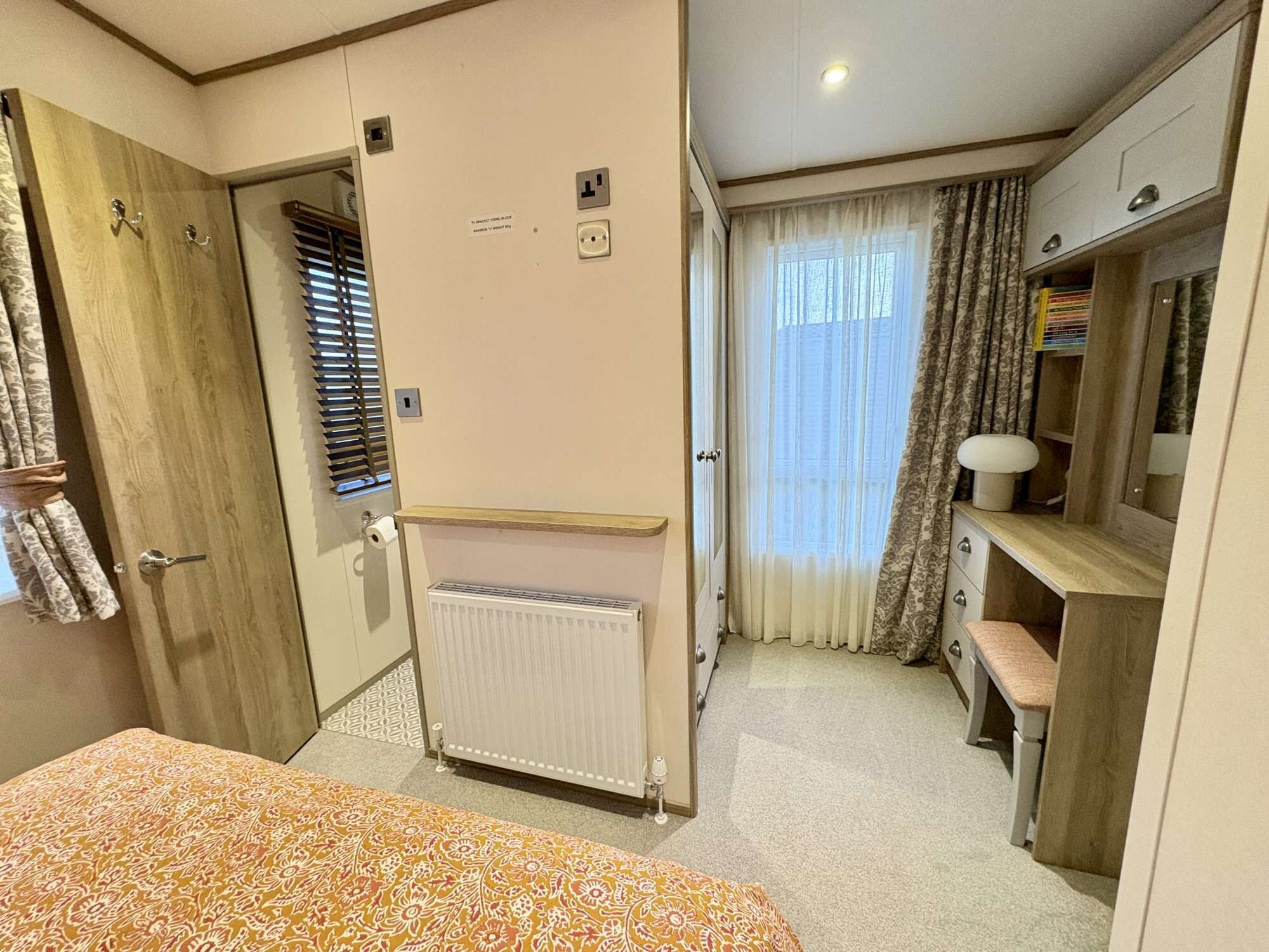 A compact bedroom with a bed, a desk, a radiator, and a window with curtains.