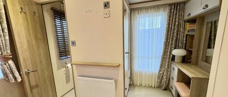 A compact bedroom with a bed, a desk, a radiator, and a window with curtains.