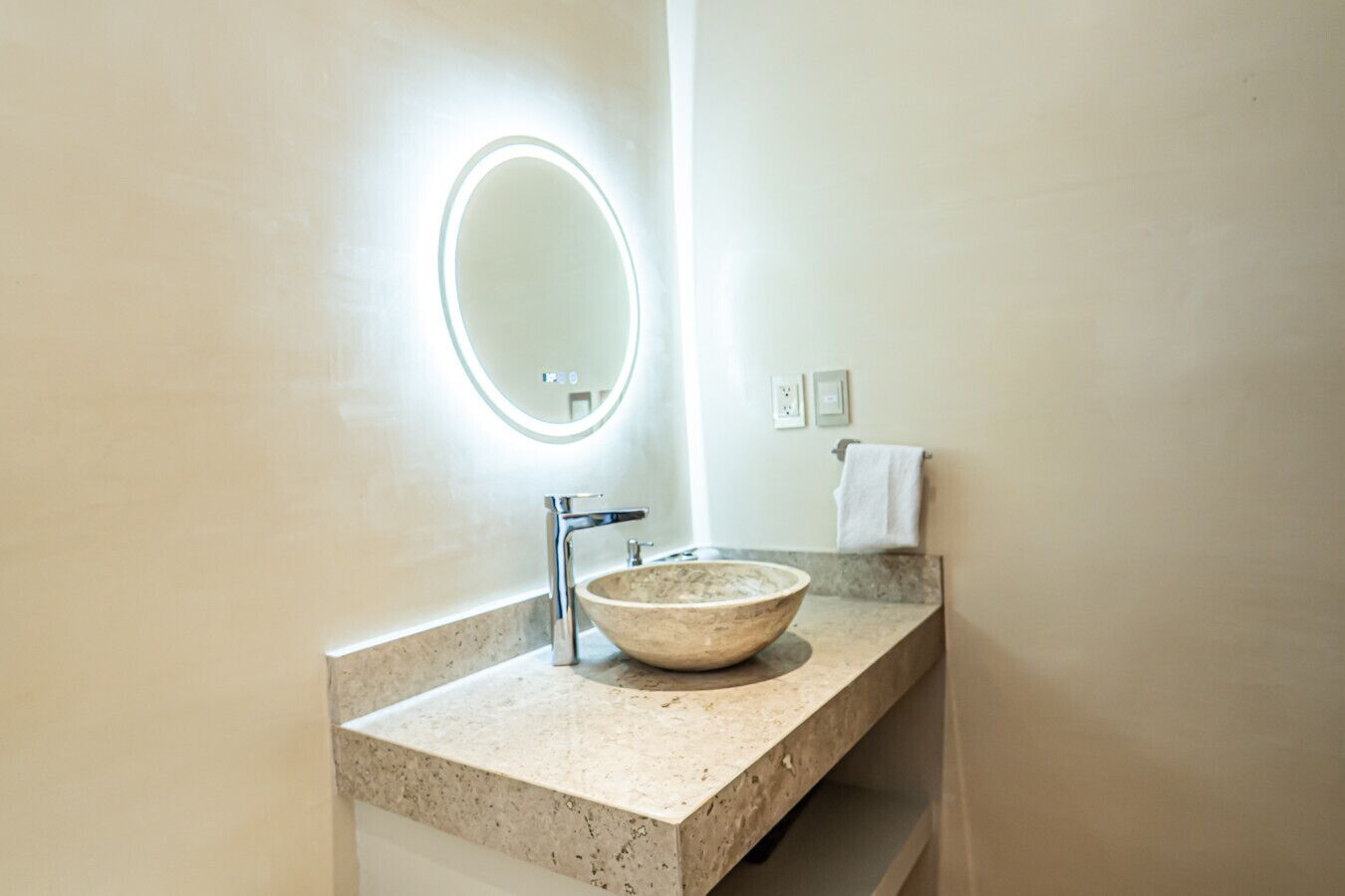 Une salle de bain avec un miroir rond, un lavabo en forme de coupe et un porte-serviettes.