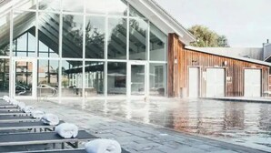 A modern building with large glass windows and a pool area with sun loungers.