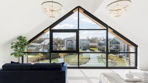 A modern room with a large skylight, a black sofa, a white bed, and a chandelier.
