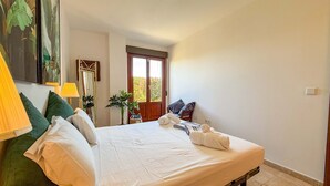 A bedroom with a bed, pillows, a lamp, a mirror, and a door leading to a balcony.