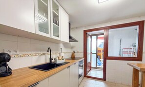 Eine Küche mit einem schwarzen Spülbecken, einer Holz Arbeitsplatte, weißen Schränken und Blick durch eine Glastür in einen Außenbereich.