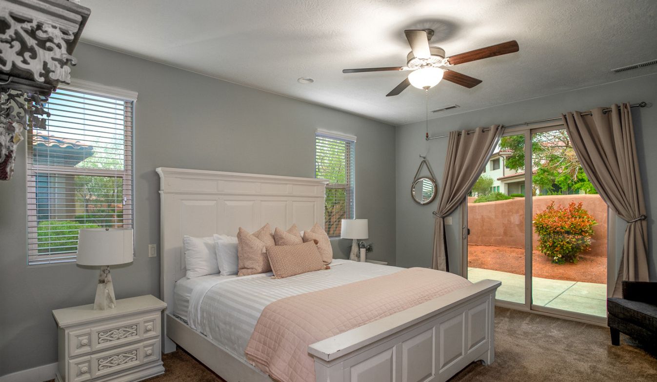 Une chambre avec un grand lit, un ventilateur de plafond, une fenêtre avec des stores et une vue sur l’extérieur.