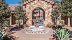 A stone fountain with multiple tiers in a courtyard surrounded by desert plants and a building with a tiled roof.