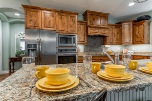 A kitchen with wooden cabinets, granite countertops, stainless steel appliances, and yellow dinnerware.