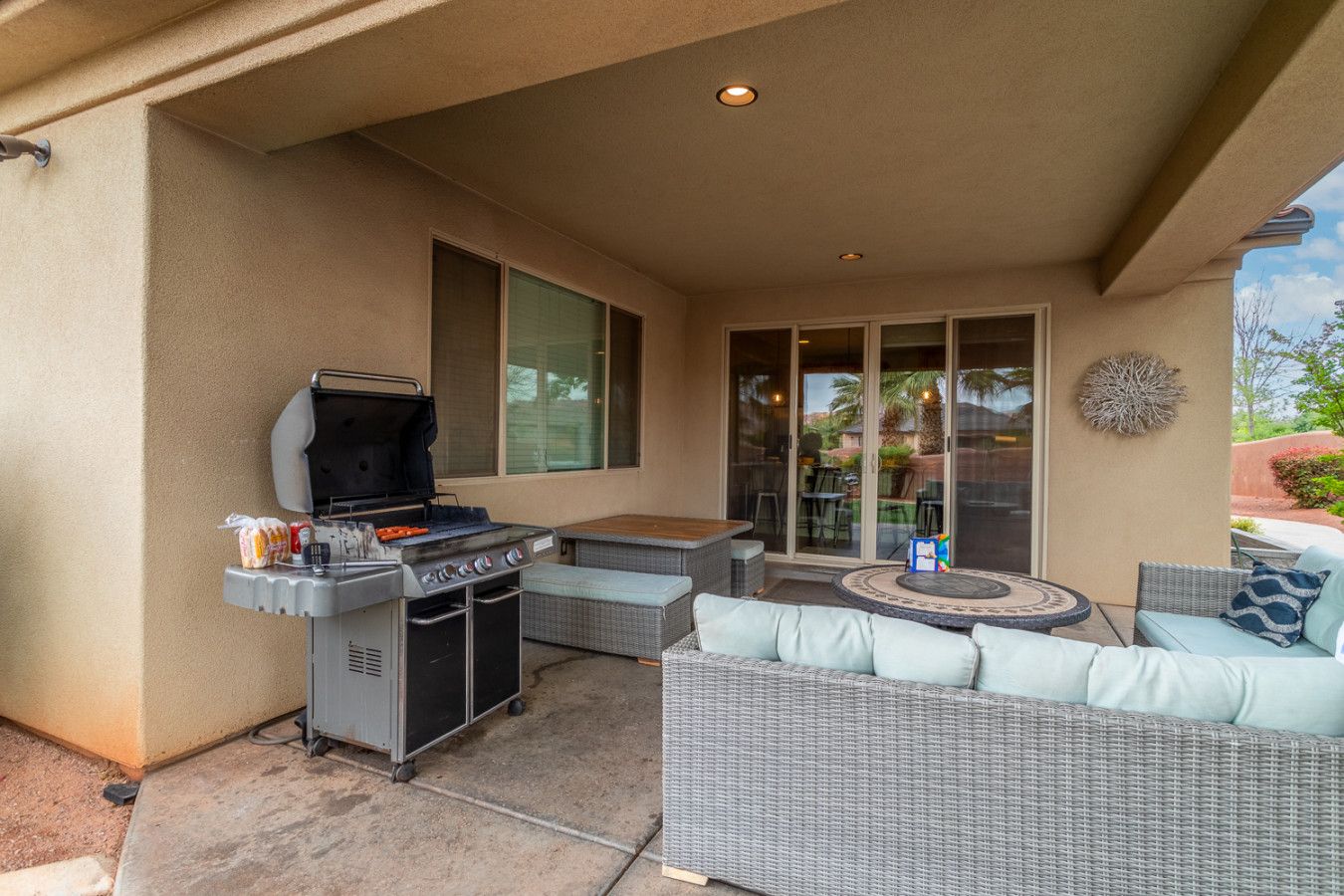 Une terrasse extérieure équipée d’un barbecue, de meubles en osier et d’une porte vitrée donnant sur un espace de détente extérieur.