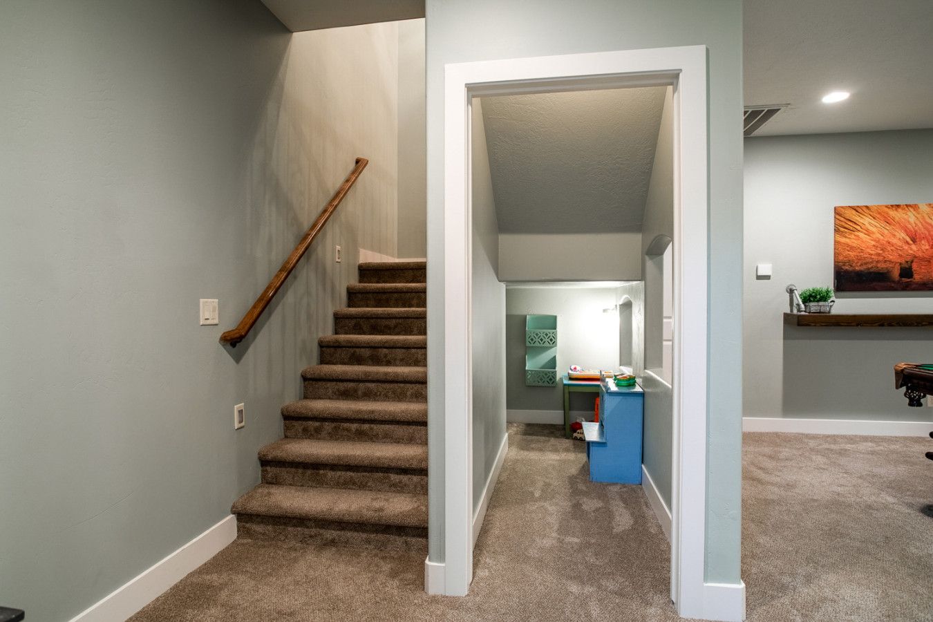 Un escalier recouvert de moquette menant à un deuxième étage, un couloir avec une armoire bleue et un tableau accroché au mur.