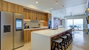 A modern kitchen with a large island, stainless steel appliances, wooden cabinetry, and a view to the outside.
