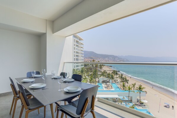 Comedor con una mesa dispuesta para cuatro personas, con vistas a una playa y una piscina.
