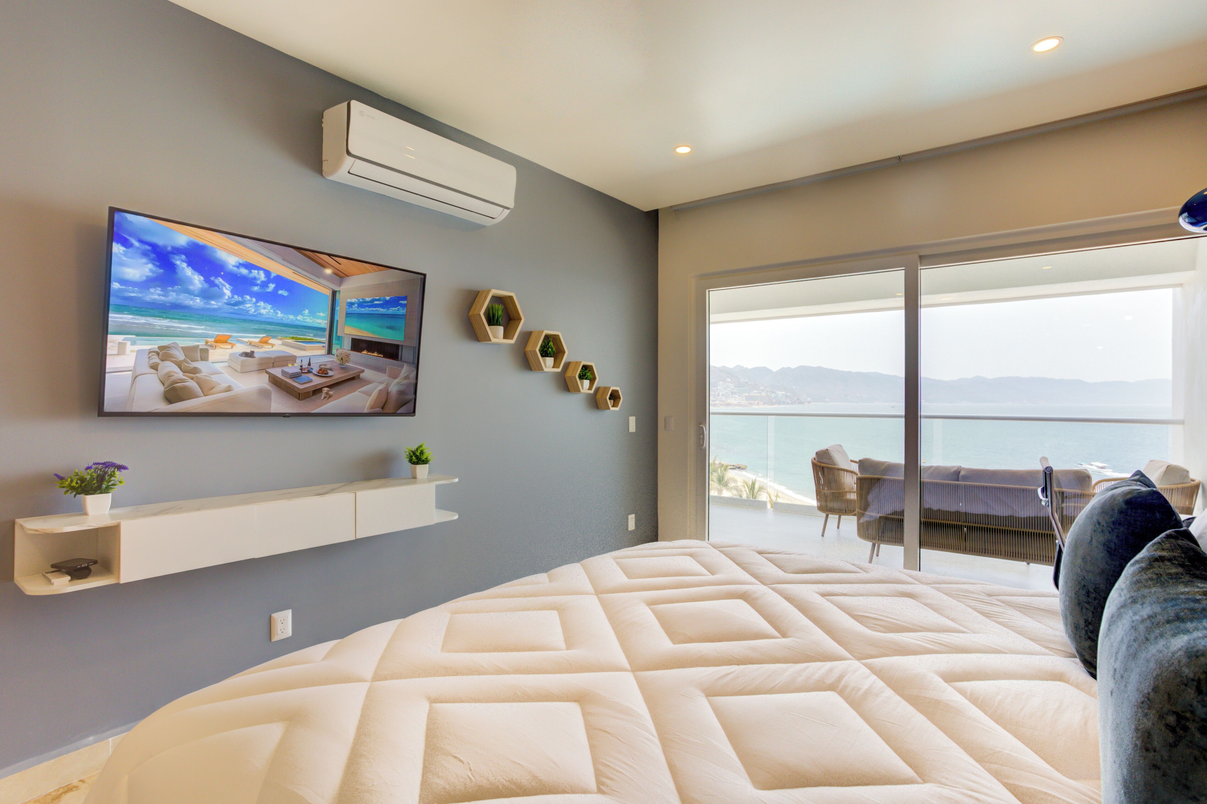 Ein modernes Schlafzimmer mit einem großen Bett, einem an der Wand befestigten Fernseher und einem Balkon mit Blick auf die Stadt.
