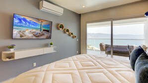 A modern bedroom with a large bed, a mounted TV, and a balcony with a view of the city.