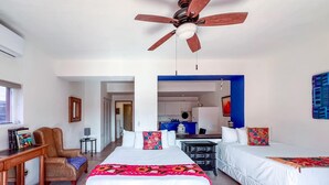 Camera d'albergo con due letti, una ventola a soffitto, una scrivania con sedia e vista sull'area cucina.