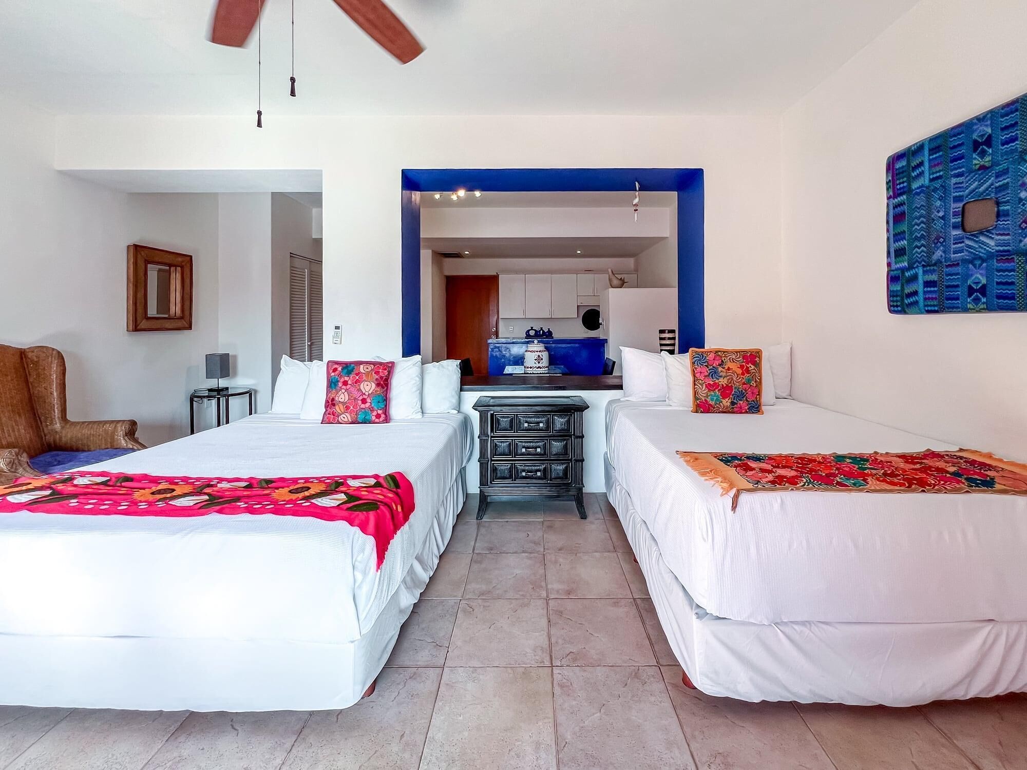 A hotel room with two beds, a desk, a chair, and a kitchenette.