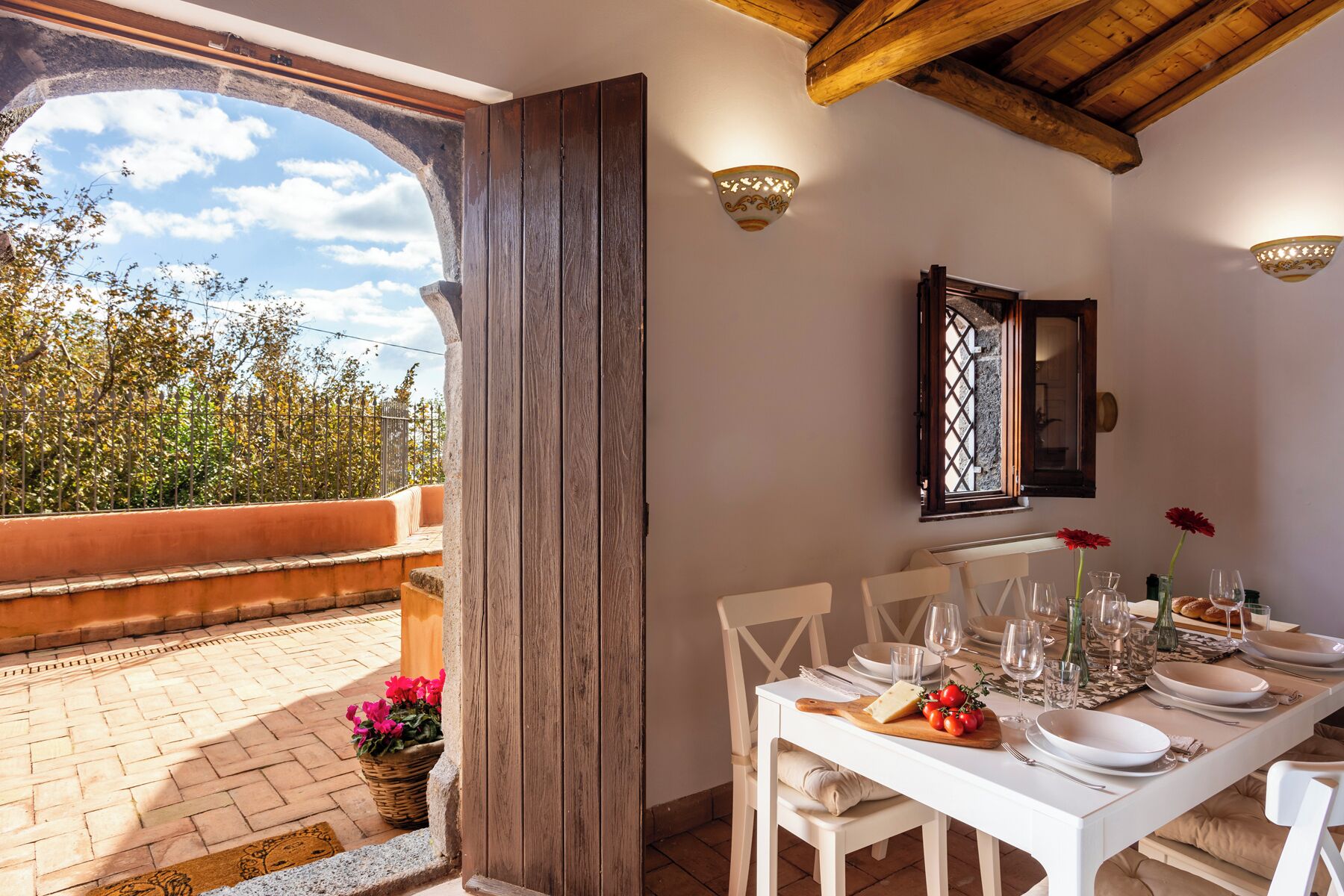 Un comedor con una mesa dispuesta para cuatro, una ventana con vista a árboles y un techo de madera.