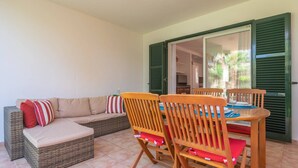 Une terrasse ensoleillée avec un canapé en osier, des chaises en bois et une table.