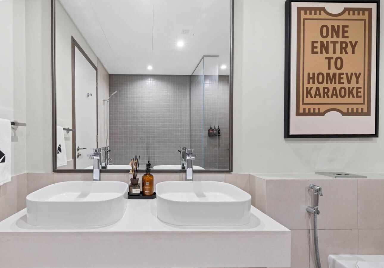 Een moderne badkamer met twee wastafels, een grote spiegel en een bordje in een lijst erboven.