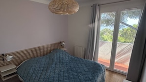 Une chambre à coucher comprenant un lit, une lampe de chevet, un luminaire suspendu et une vue sur l’extérieur grâce à une porte coulissante.