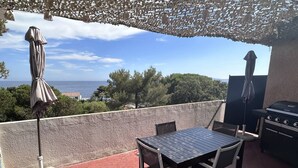 Un balcon avec une table et des chaises, un barbecue et des parasols.