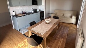 Une cuisine moderne avec des meubles gris, une table à manger en bois et un canapé beige dans un espace de vie lumineux.
