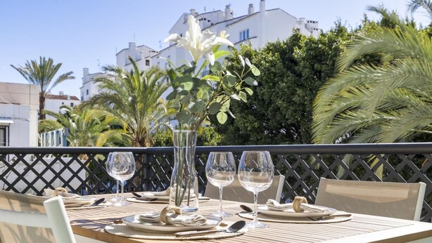 A dining table set outdoors with a view of buildings and greenery in the background. - Apartment in Terrazas de Banús for 4 people |4-12 (Puerto Banús - Marbella)