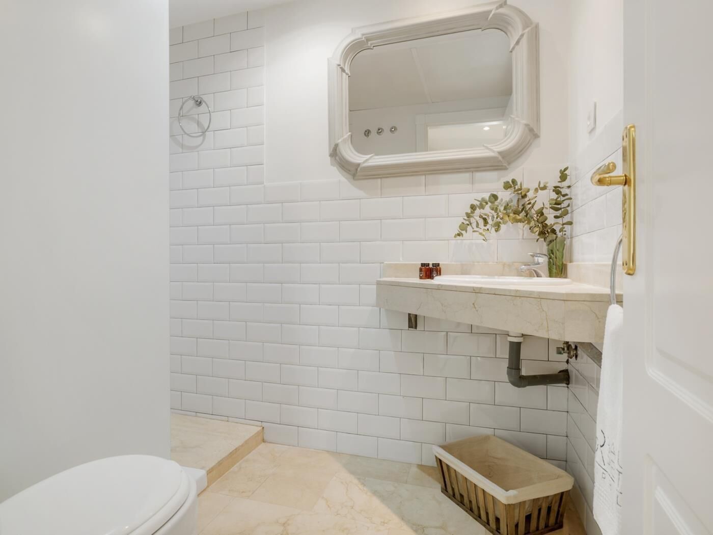 Un bagno con piastrelle bianche a metro, un water bianco, un lavabo con piano in marmo e una piccola panca in legno.