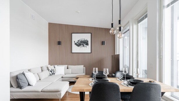 A modern dining area with a wooden table, black chairs, and a grey sofa.