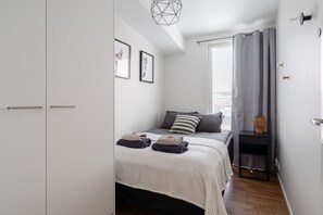 Un dormitorio con cama, armario, ventana con cortinas y una lámpara con forma geométrica.