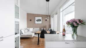 A modern kitchen with a dining area, featuring a wooden wall panel, a white sofa, and a vase of flowers.