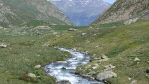 A mountain landscape with a flowing river, rocky terrain, and a small hut.