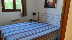 A bedroom with a striped bedspread, a bedside table with a lamp, a radiator, and a window with curtains.