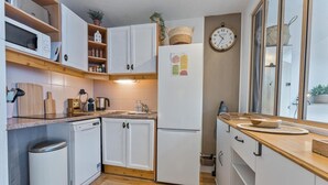 Une cuisine moderne avec des meubles blancs, un lave-vaisselle encastré, un réfrigérateur, un plan de travail en bois et une horloge murale.